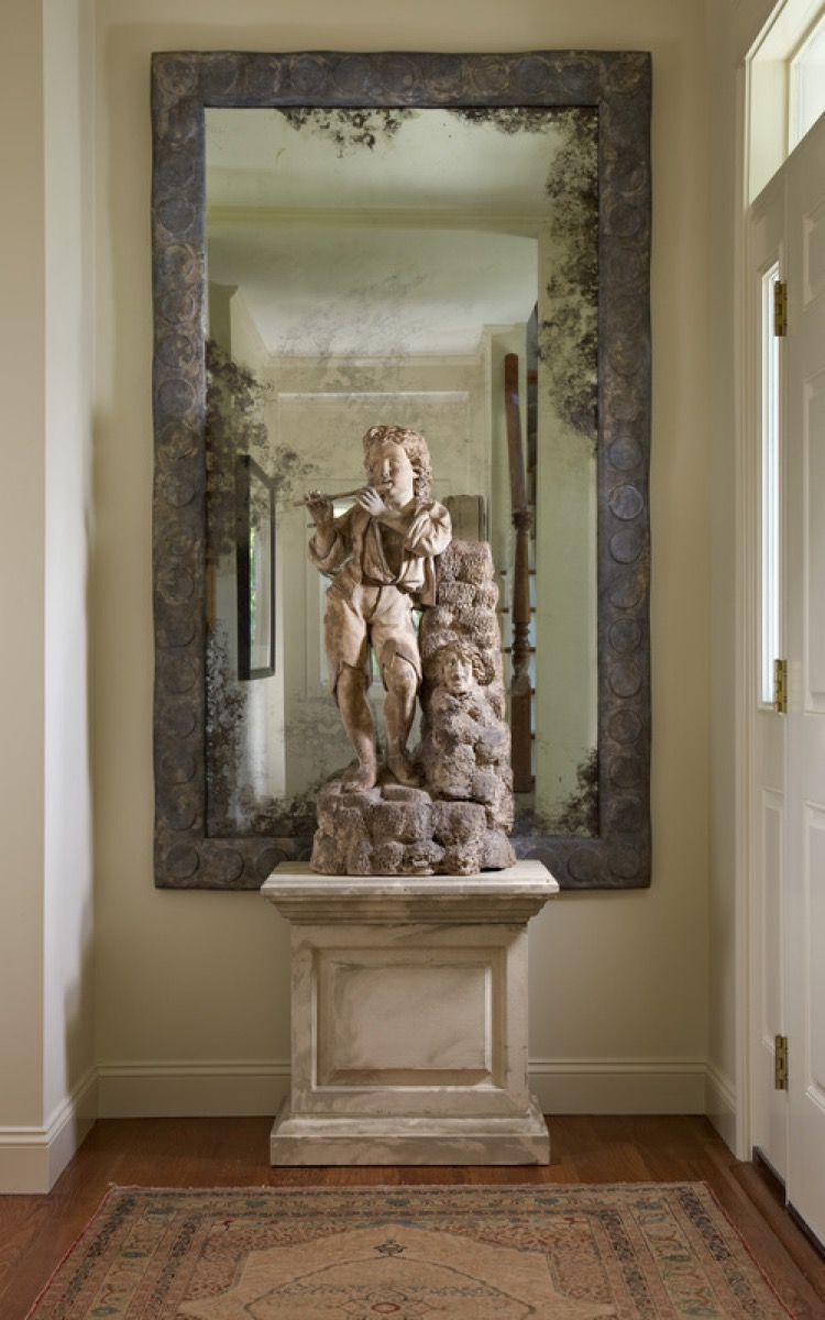 Antique carved stone figure on a pedestal before a distressed mirror in the vestibule of Villa Medina