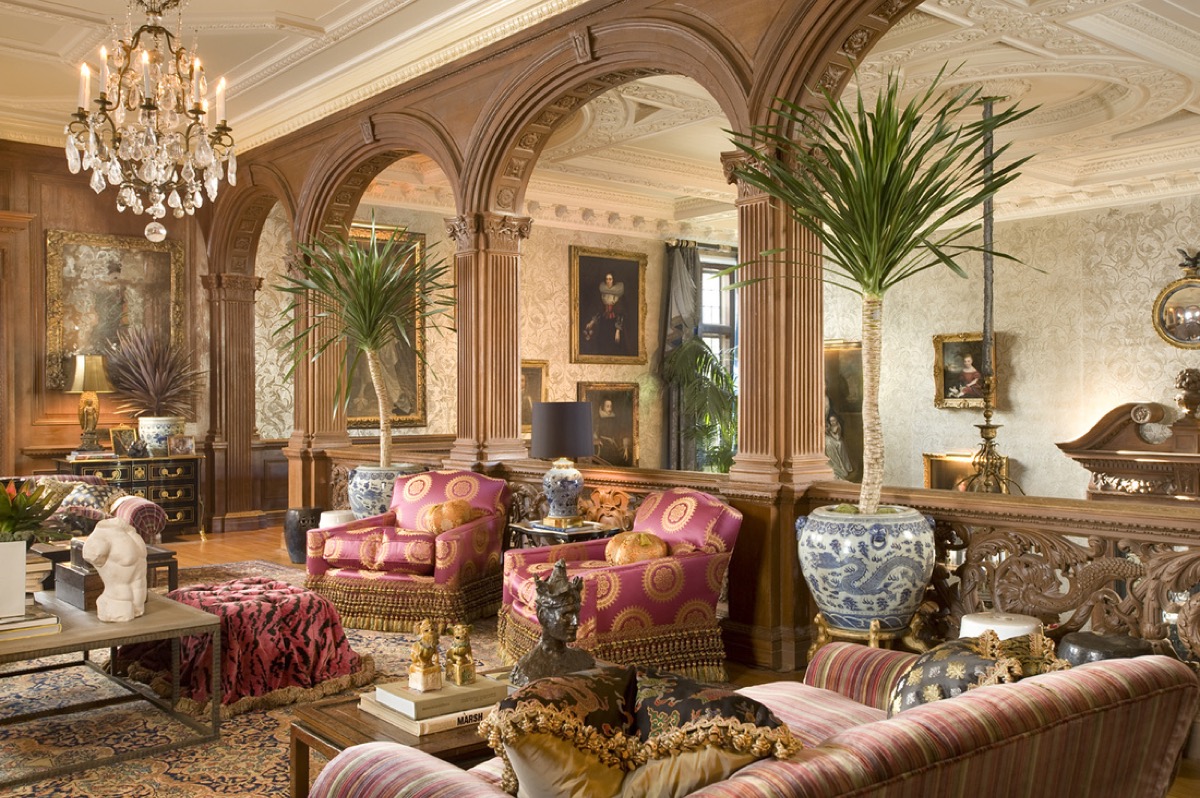 Wood paneled classical salon with an arched colonnade, silk armchairs and blue and white porcelain beneath a chandelier
